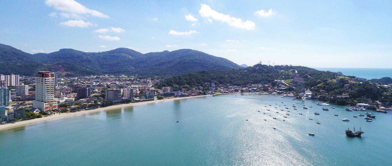 Vista aérea do George VI Residencial em uma baía em meia-lua, com o skyline de Itapema ao fundo